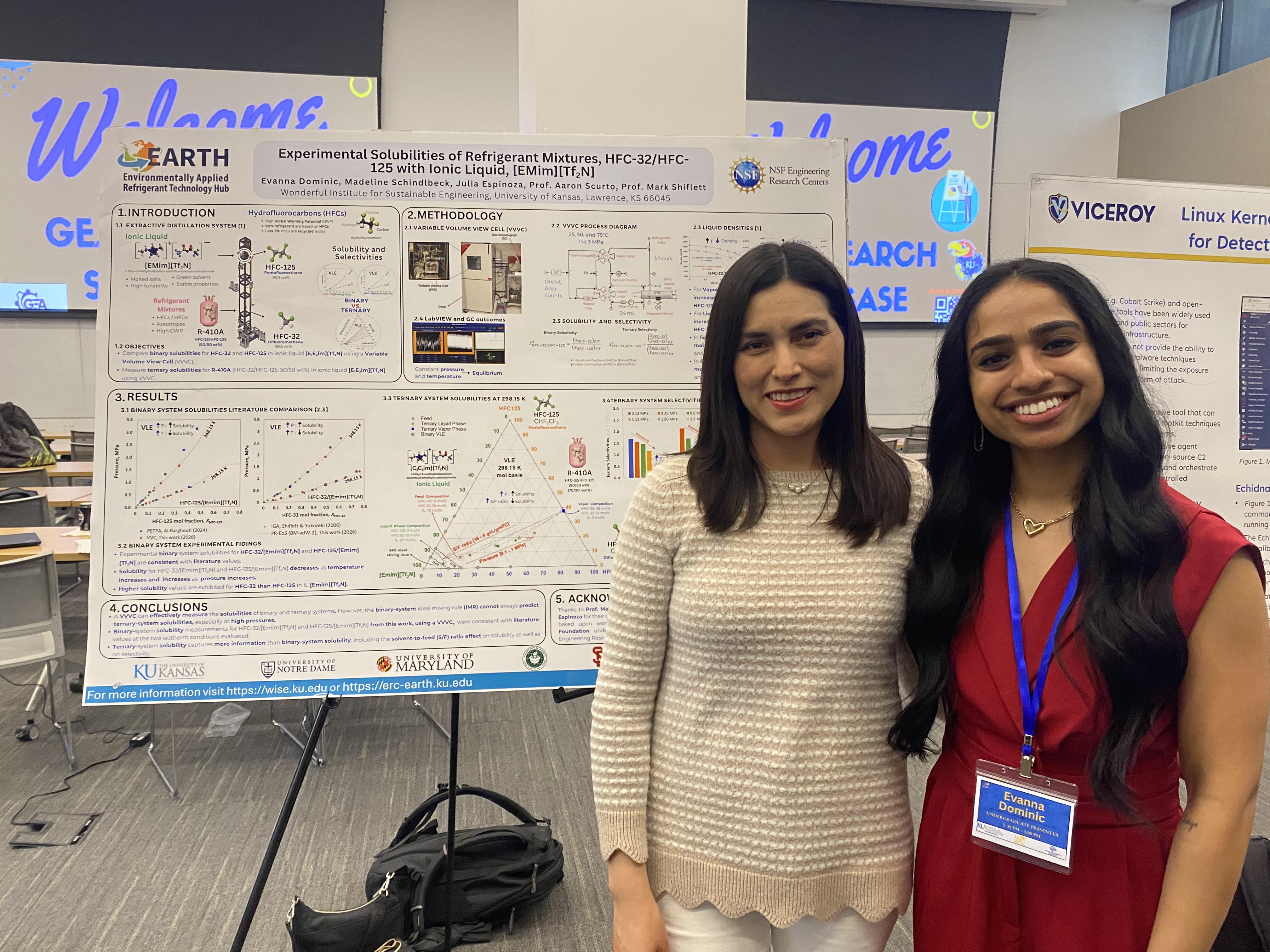 two people stand next to research poster