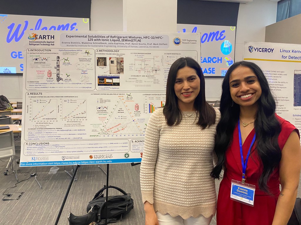 two people stand next to research poster